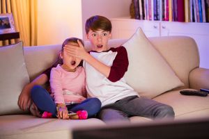 Brother covering surprised sisters eyes watching TV in living room