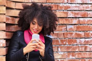 Beautiful young woman leaning against a brick wall typing message