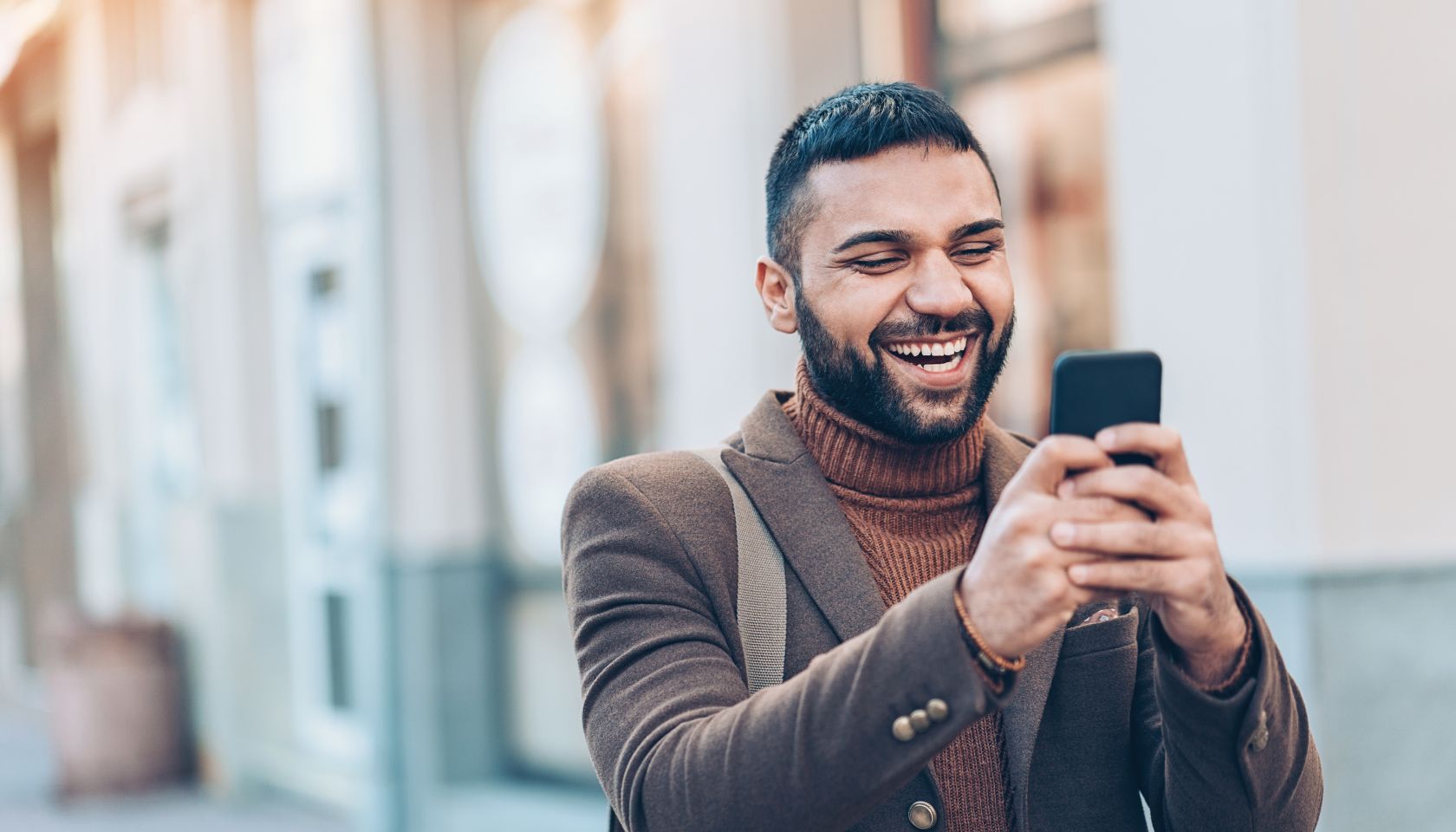 Smiling man with smart phone outdoors in the city