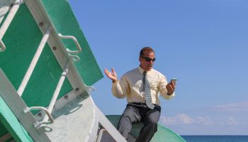 Businessman looking at mobile phone drifting on a buoy out at sea
