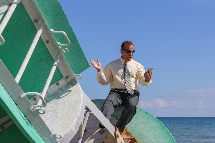 Businessman looking at mobile phone drifting on a buoy out at sea