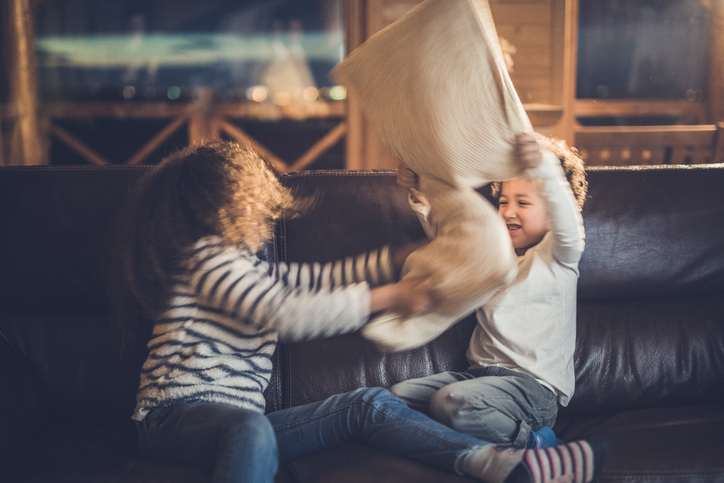 Playful black kids having fun while fighting with pillows at home.