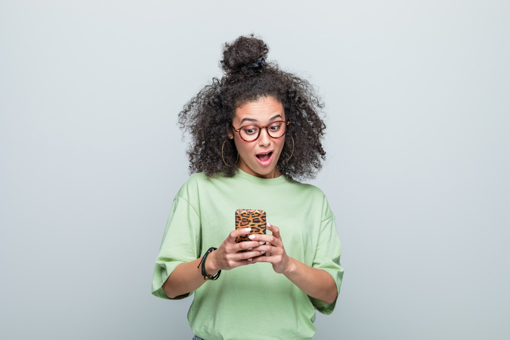 Portrait of surprised young woman using phone