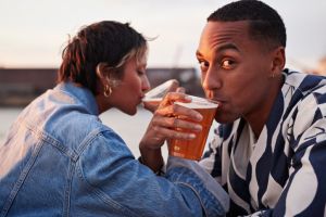 Young man drinking beer with girlfriend hand in hand