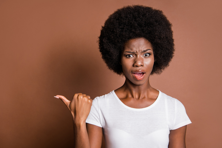 Photo of questioned attractive dark skin girl open mouth indicate thumb empty space isolated on brown color background