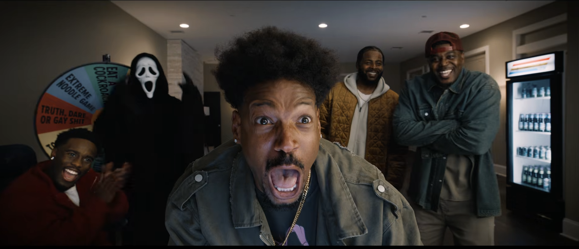 A group of people in a room, including a person with an afro hairstyle making a surprised facial expression, and two other men standing behind them.