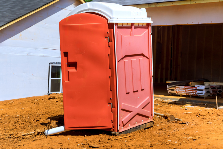 Construction site includes portable toilet in yard near building structure