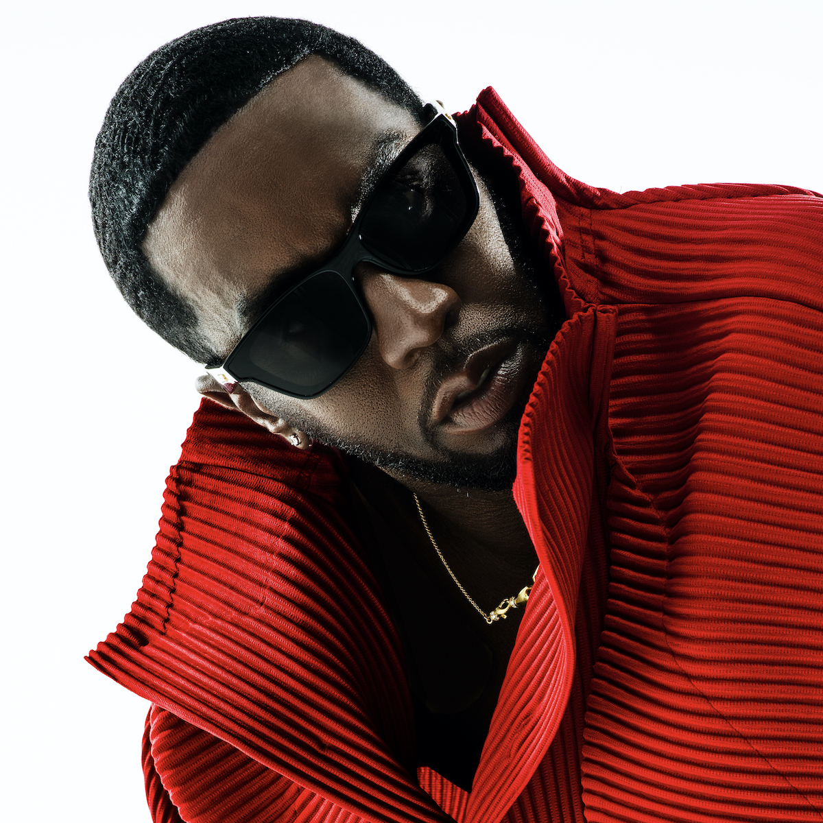 A person wearing a red pleated jacket and sunglasses, with a serious expression on their face.
