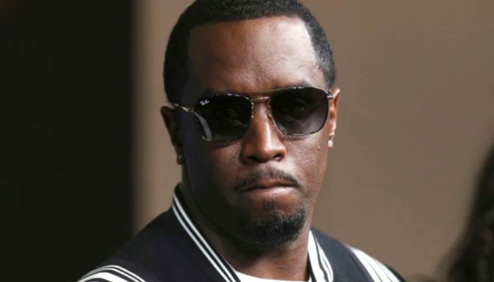 A man wearing sunglasses and a black and white striped shirt, with a serious expression on his face.
